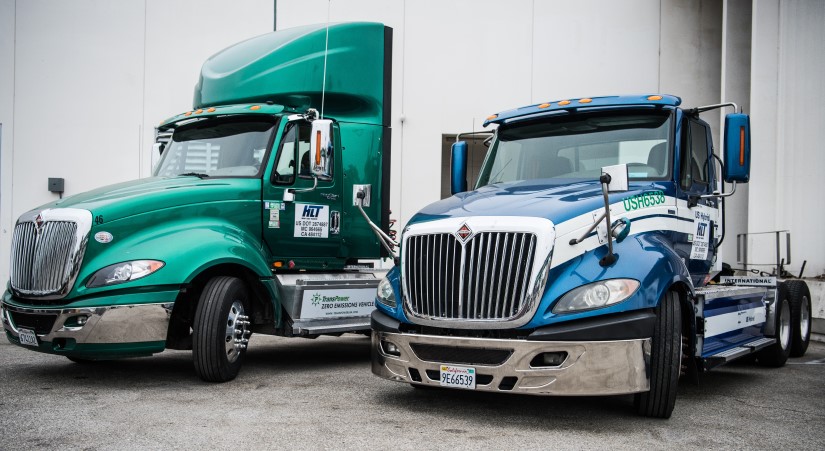 Two heavy-duty semi trucks, one green and one blue, are parked next to each other. 
