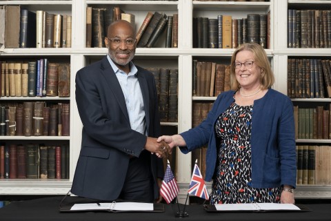 A man and a woman shake hands in front of a bookcase