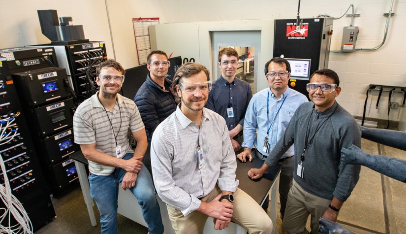 Six men stand in a laboratory.