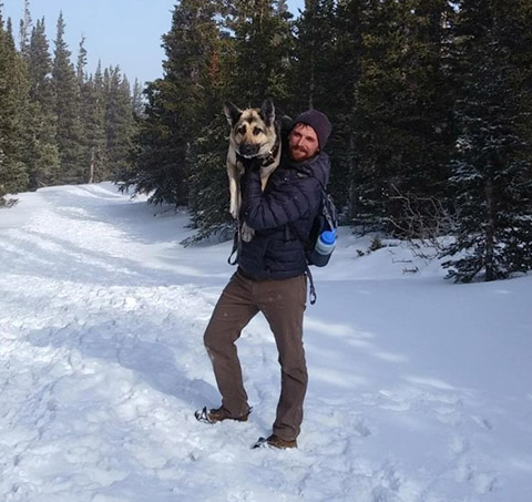 Photo of a man holding a dog on a snow-covered trail in a forest