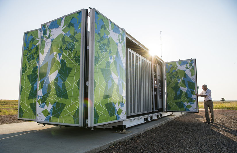 Photo of a large stationary battery energy storage unit with a man holding open a door of the unit