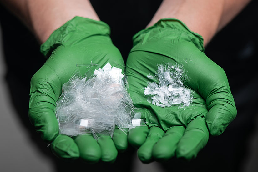 Two gloved hands each holding pieces of polyester, in one hand before enzymatic degradation, and in the other hand after enzymatic degradation