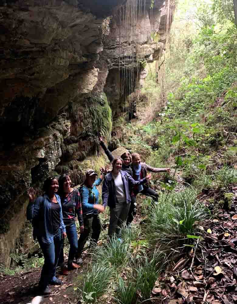 Six women hiking under a mossy cliff