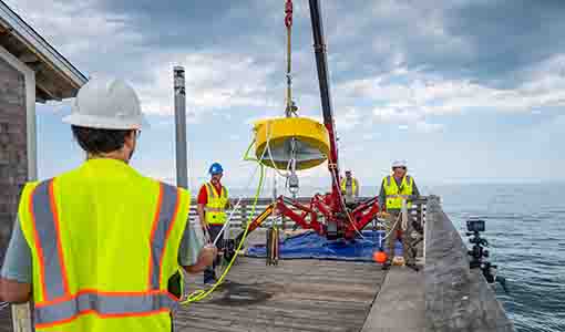 Researchers use a crane to lift a yellow buoy float into the water.