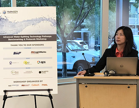 Photo of a woman speaking at a podium next to a display poster