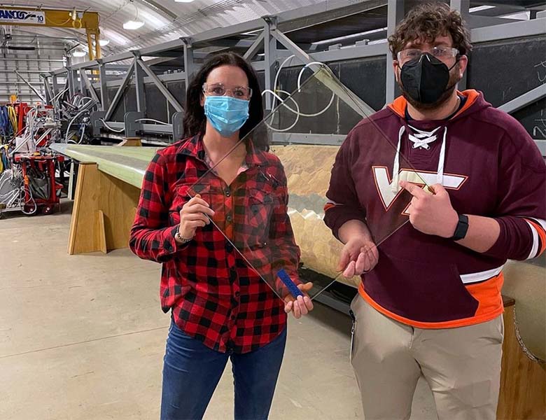 Two researchers standing in a warehouse and holding a rectangle of clear plastic