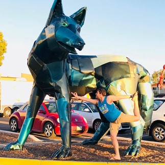 Nic Rorrer performs a yoga pose in front of a large metal sculpture of a fox
