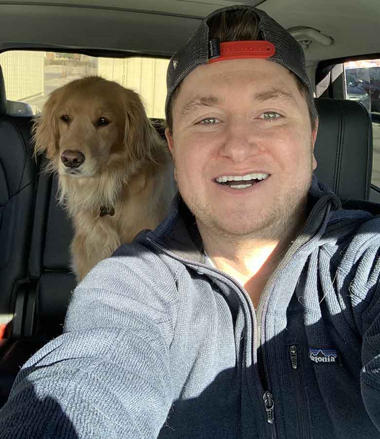 A selfie of Aaron Levine sitting in his car with a golden retriever in the back seat.