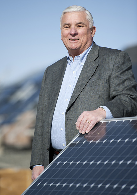 Photo of a man standing outside with his hand on a solar panel