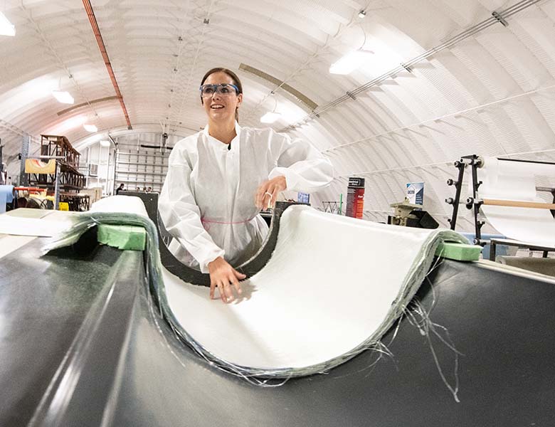 Robynne Murray in a white jumpsuit and goggles standing above a large wind turbine mold.