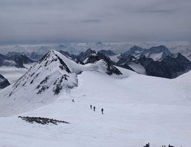 Mountains with six small figures skiing through the snow.