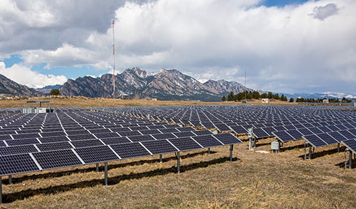 Solar panels in the foreground with mountains in the background.