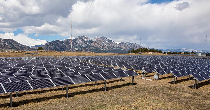 Solar panels in the foreground with mountains in the background.