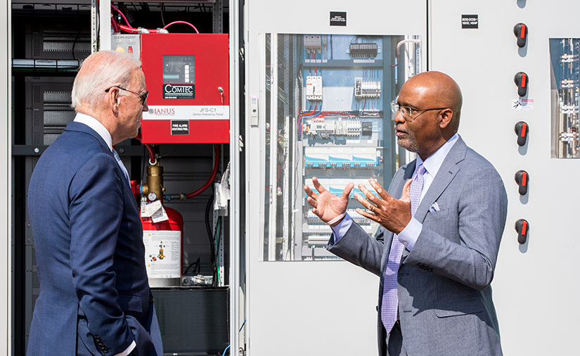 Two men speak outside next to electrical equipment