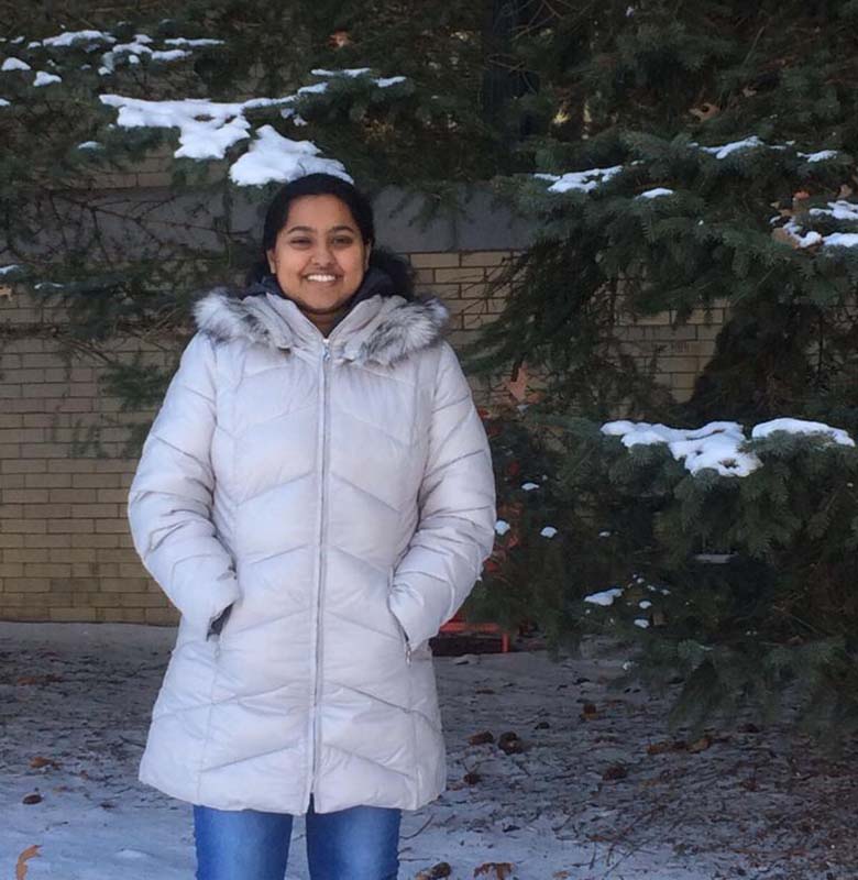 A woman in a winter coat standing in front of a snowy evergreen tree.