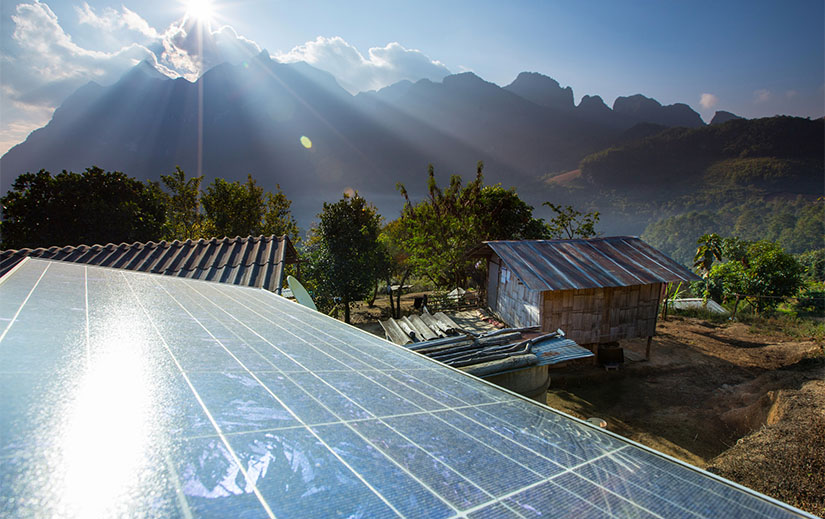 Solar panels in the foreground with buildings, trees, and mountains in the background.