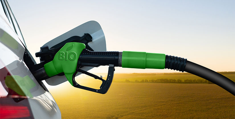 A fuel nozzle fills a car’s fuel tank with biofuel with fields in the backdrop.