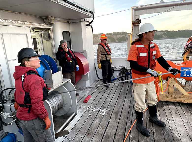 Four researchers in hardhats standing on the deck of a boat.