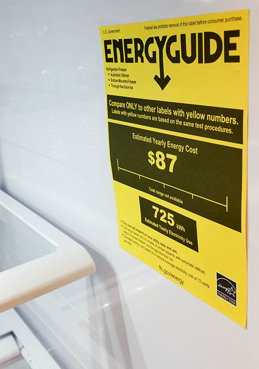 the front of a refrigerator with a yellow paper showing the Energy Guide rating, or the energy efficiency of the appliance. 