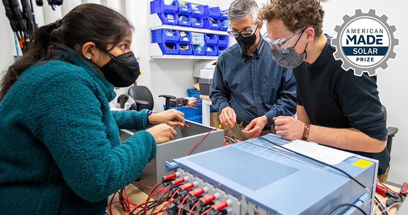 Three people wearing masks work on a solar device on a table in a laboratory.