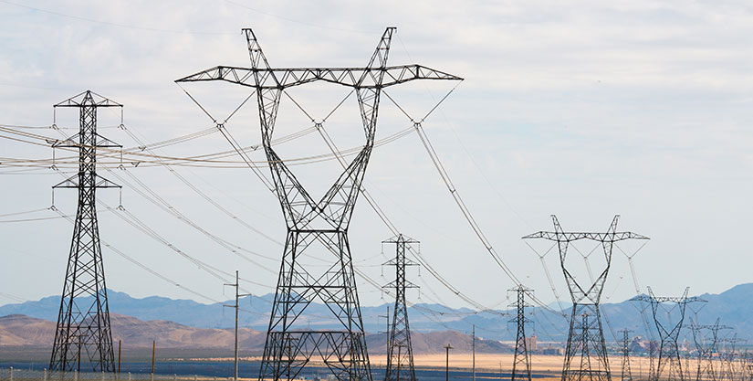 Photo of transmission towers with a solar farm nearby and desert and mountains in the background.