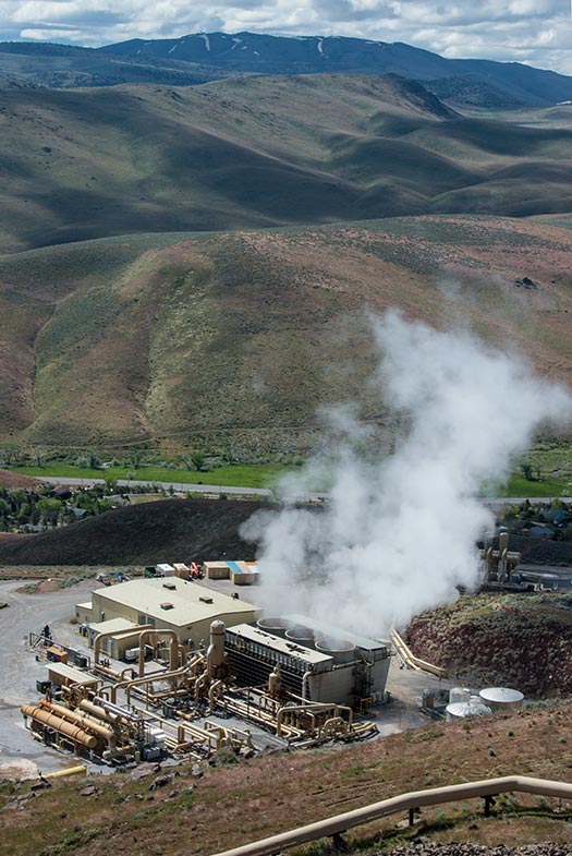An aerial image of a geothermal plant with mountains in the background.
