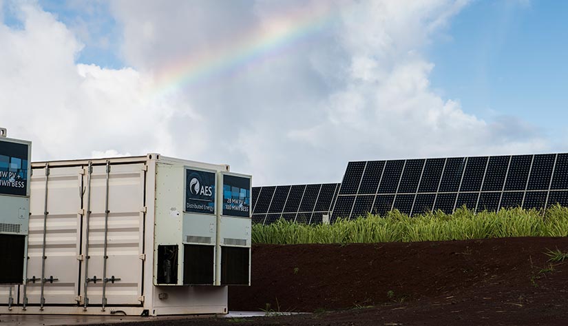 Photo of energy storage with solar panels in the background, showing that storage and solar tend to go well together operationally.
