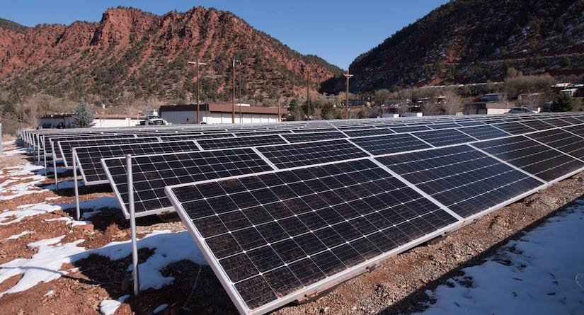 Rows of solar panels sit underneath red sandstone cliffs in the rural western United States.