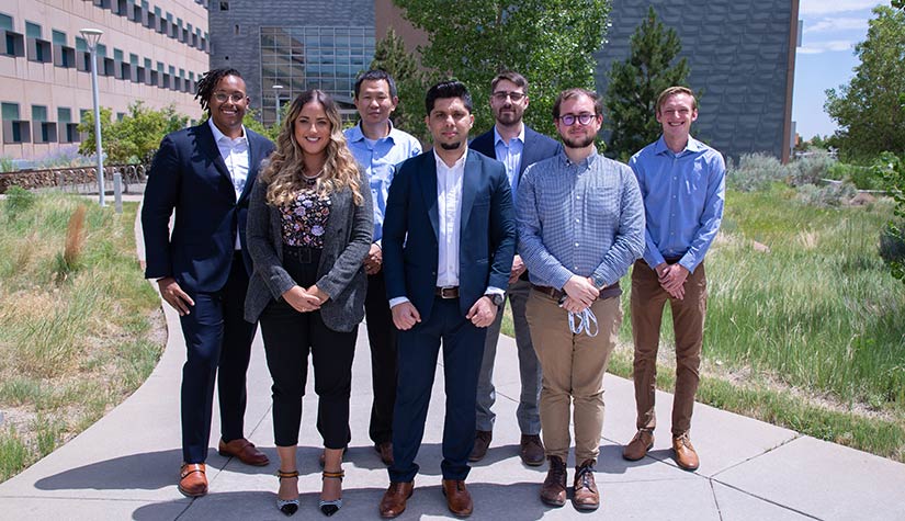 A group of seven people pose in front of a building on the NREL campus in Colorado.