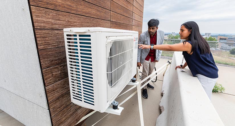 Researchers outside of a modular home inspecting a heat pump.