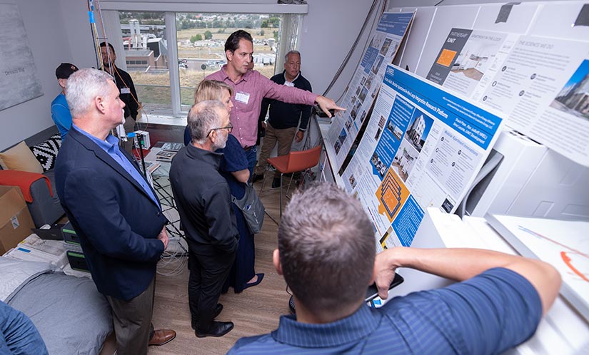 A man in the center of a room points at a research poster as several other people look on and listen.