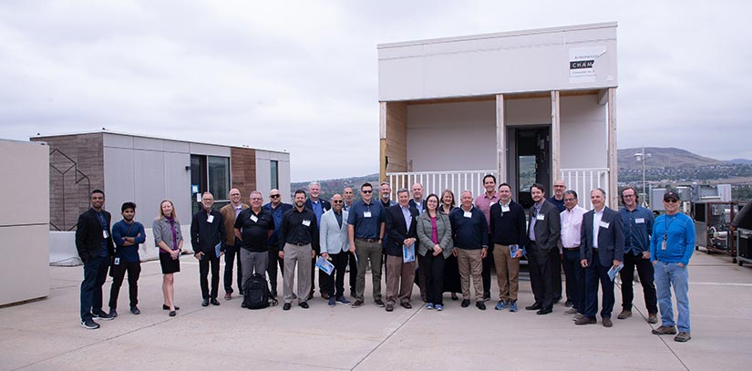 A group of people posing for a photo in front of two rectangular housing units.