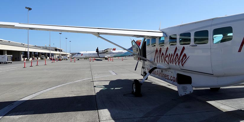 A Mokulele airplane sits on the tarmac at a small airport.