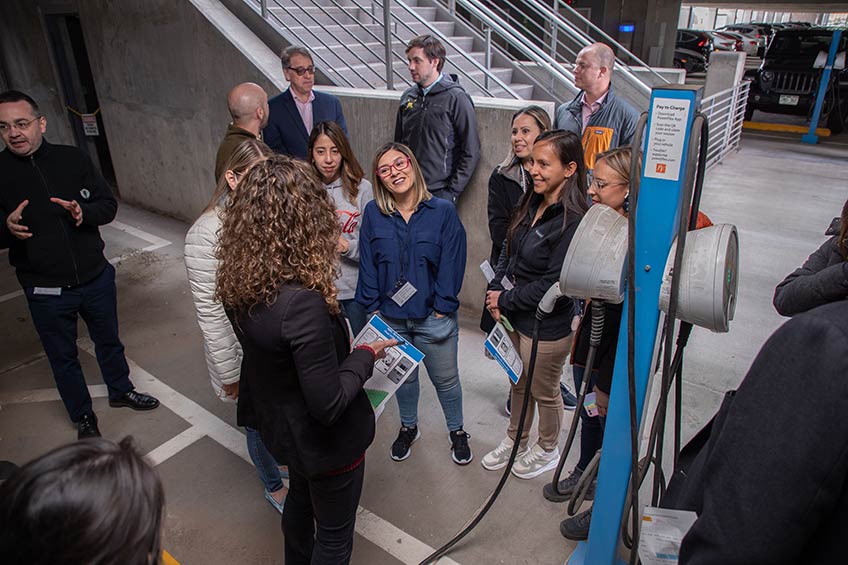 People stand together laughing and smiling in a parking garage with an electric vehicle charger next to them.