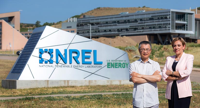 An NREL scientist and the CTO of Cemvita Factory stand in front of the welcome sign at the main campus of the National Renewable Energy Laboratory, with buildings and facilities in the background.