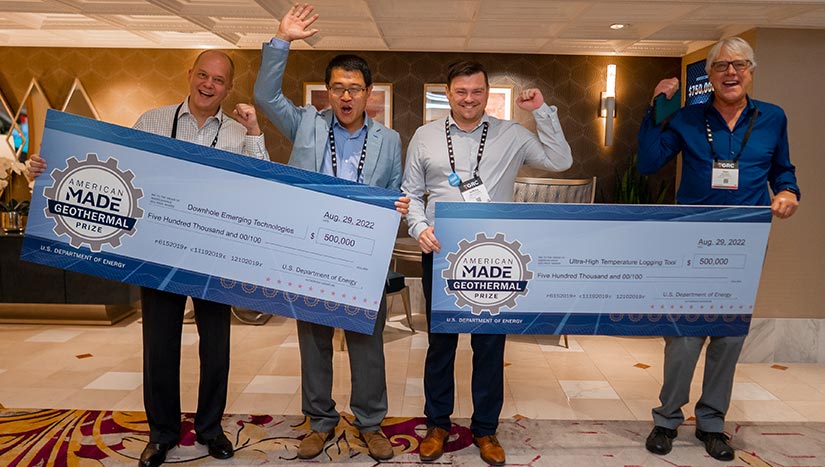 Four people cheering and holding two giant checks.