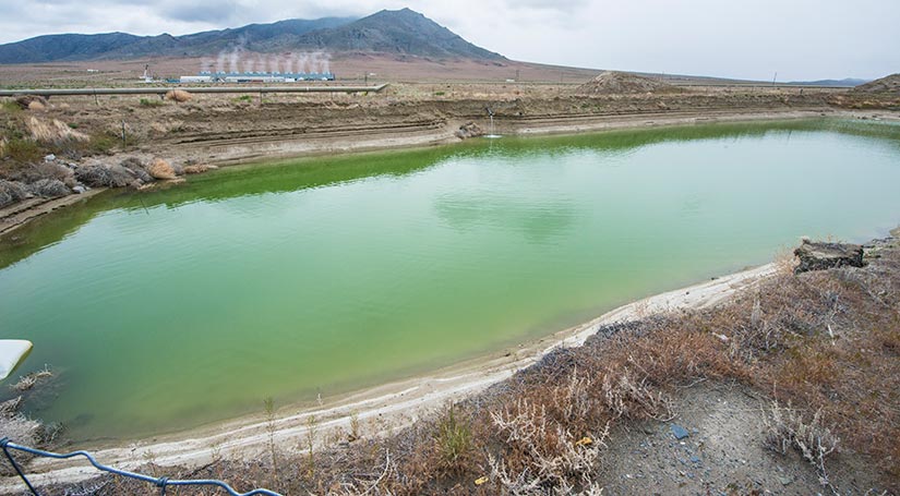 Geothermal reservoir beside plant emitting steam.