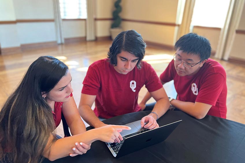 Three students look at a computer screen and edit a presentation.