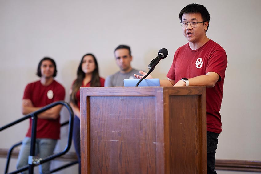 Student speaks at a podium with three other teammates waiting behind him.