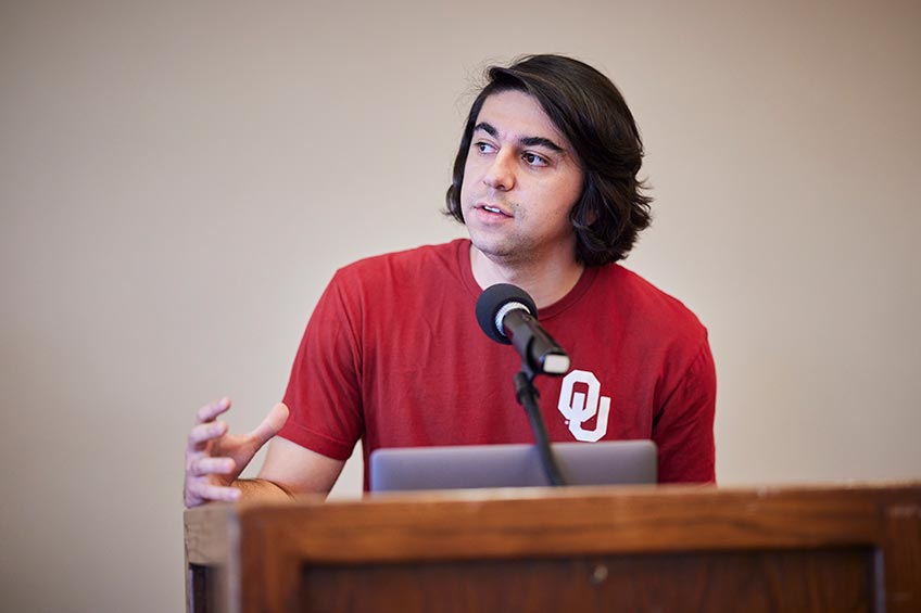 Student wearing a University of Oklahoma shirt speaks at a podium on stage.