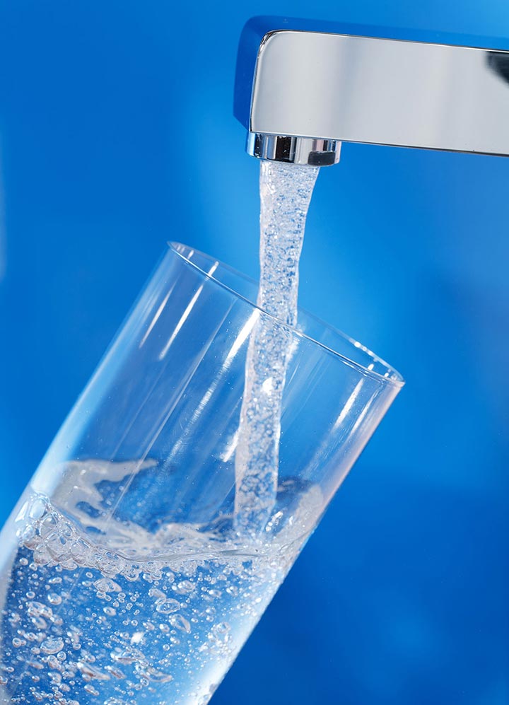 Photo of a water faucet filling a glass with water.