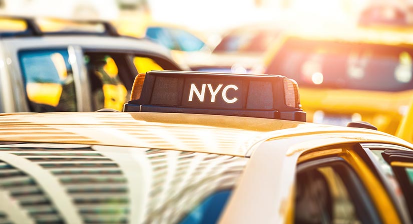 Top of a yellow taxi cab in traffic with NYC on the rooflight.