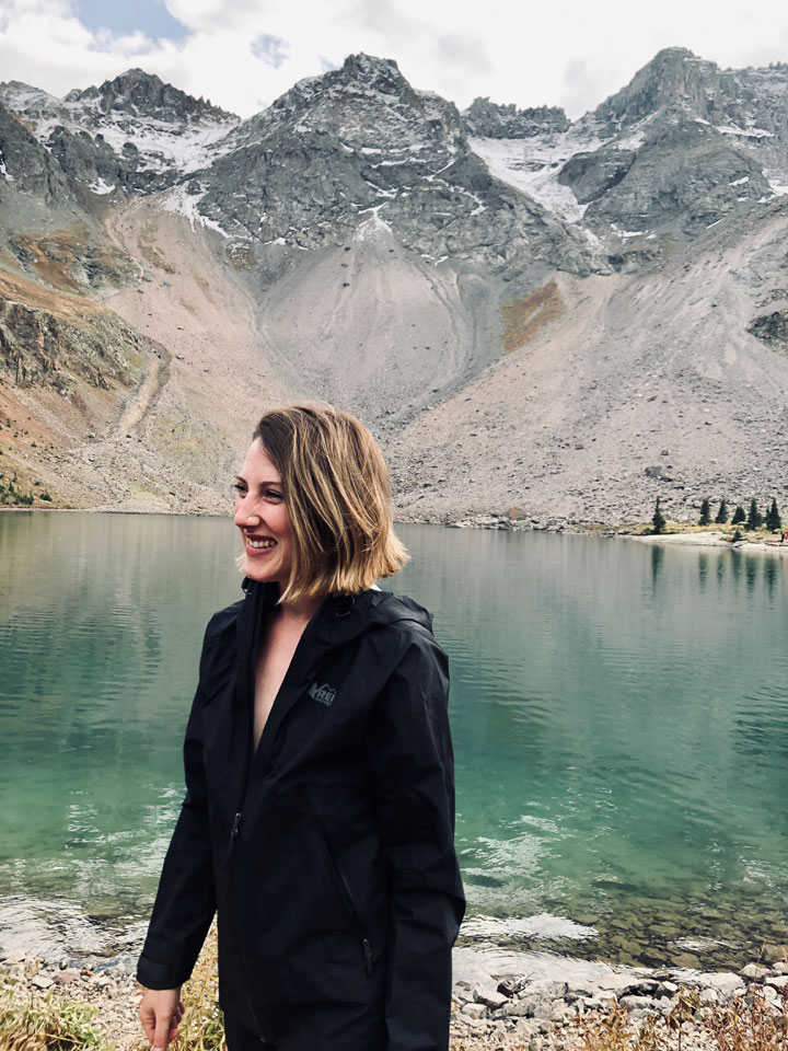 Photo of a woman standing in the mountains with a lake in background