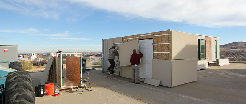 Two researchers place a panel onto an affordable home.