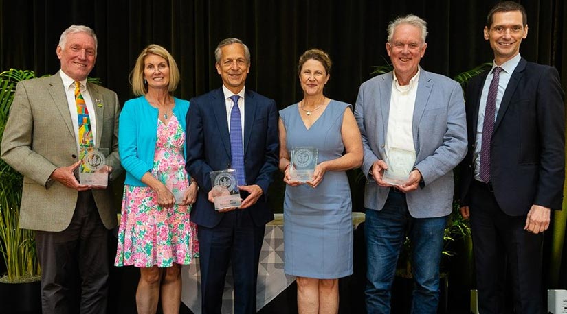 A group of people pose for a picture on stage with their trophies at an awards ceremony.