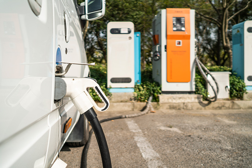 A white commercial vehicle charges at a brightly colored outdoor charging station.