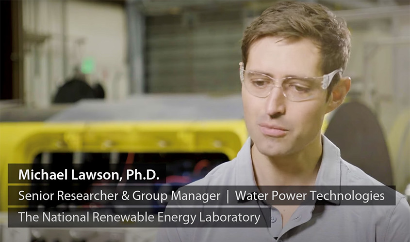 Michael Lawson talks while wearing clear goggles and sitting in a warehouse in front of mechanical equipment overlain by his name and title.