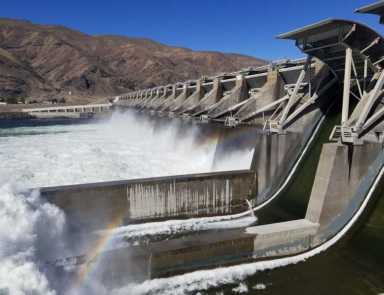 Water rushing through a hydropower dam with a rainbow in front and a mountain in the background