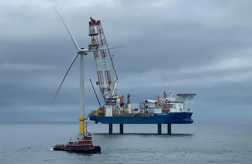 An offshore wind turbine in the ocean next to a tugboat and installation vessel.