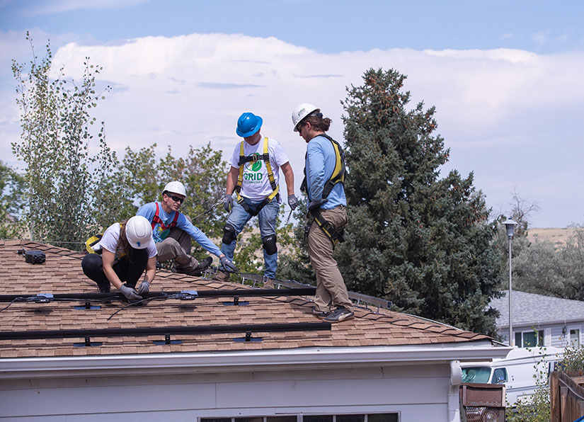 A group of people installing solar panels on the roof of a home. 